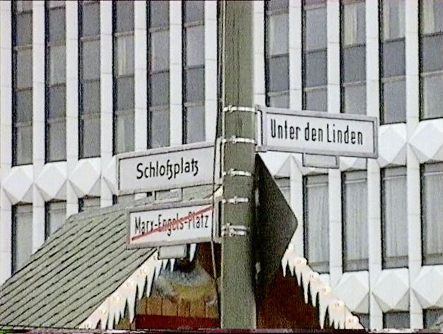 Filmstill aus „Die leere Mitte“ von Hito Steyerl. Straßenschilder in Berlin: Schlossplatz, Unter den Linden und durchgestrichen Marx-Engels-Platz. 