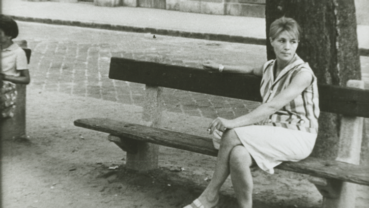 Filmstill aus ENCOUNTER: Eine junge Frau in sommerlichen Kleidung sitzt auf einer Bank und blickt sehnsüchtig in die Ferne.