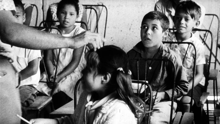 Film still from POR PRIMERA VEZ: A group of children are listening to someone.