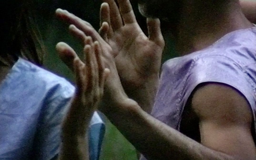 Still from the film "Afterwater" by Dane Komljen. A close-up of the hands and torsos of two standing bodies.