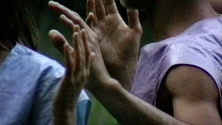 Still from the film "Afterwater" by Dane Komljen. A close-up of the hands and torsos of two standing bodies.