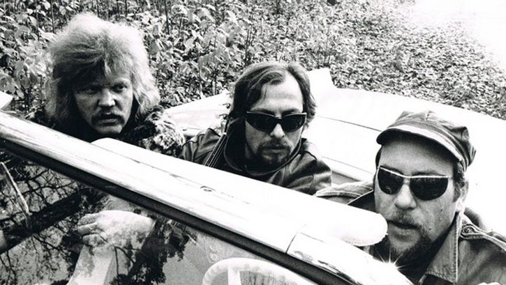 Filmstill aus AUF SCHEISSER SCHIESST MAN NICHT. Drei Männer in Lederjacken und Sonnenbrillen sitzen in einem Auto ohne Verdeck.