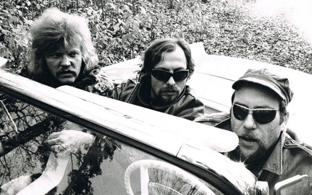 Filmstill aus AUF SCHEISSER SCHIESST MAN NICHT. Drei Männer in Lederjacken und Sonnenbrillen sitzen in einem Auto ohne Verdeck.