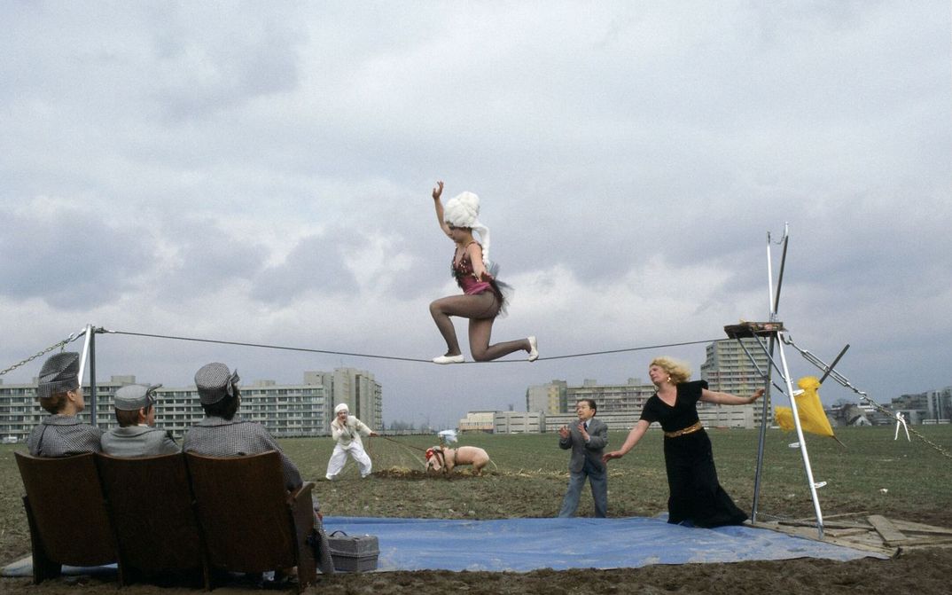 Filmstill aus BILDNIS EINER TRINKERIN: Auf einem leeren Feld tritt eine Seiltänzerin auf. Im Hintergrund sind Hochhäuser zu sehen.