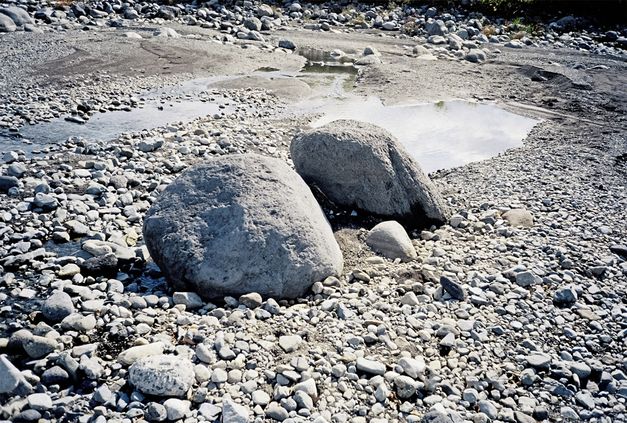 Still from the film "Ishi ga aru" by Tatsunari Ota. Two large stones sit in the centre of the image, on top of a landscape covered in grey stones.