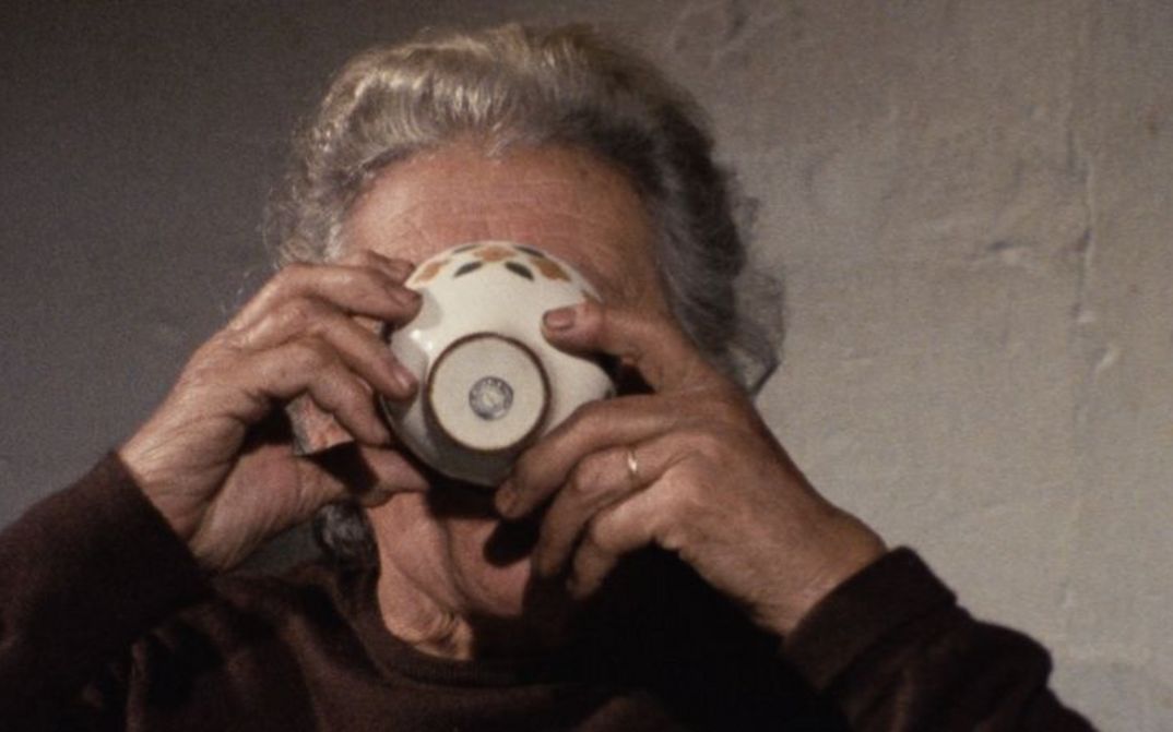 Filmstill aus O MOVIMENTO DAS COISAS: Eine Frau trinkt aus einer Tasse, die ein Teil ihres Gesichts verdeckt.