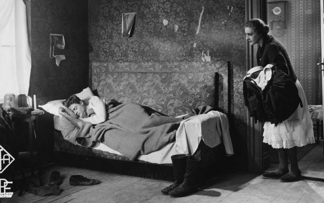 Filmstill aus ZUFLUCHT. Eine Frau blickt in ein Zimmer, in dem ein Mann im Bett schläft.