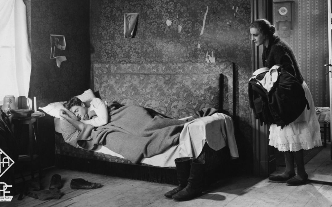 Filmstill aus ZUFLUCHT. Eine Frau blickt in ein Zimmer, in dem ein Mann im Bett schläft.