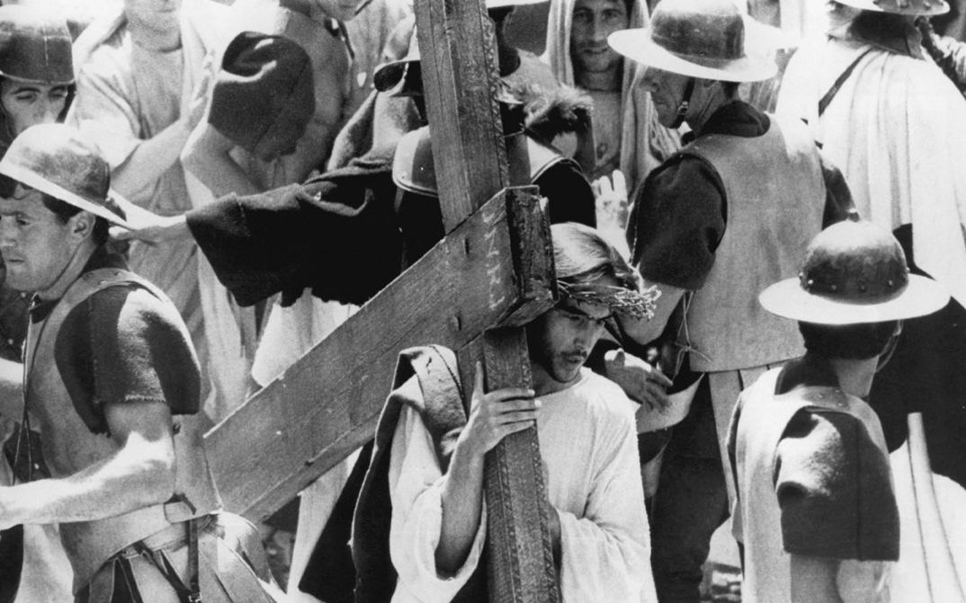 Filmstill aus IL VANGELO SECONDO MATTEO. Jesus trägt inmitten einer Menschenmenge sein Kreuz.