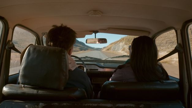 Blick von hinten auf zwei Personen im Auto auf einer Landstraße.