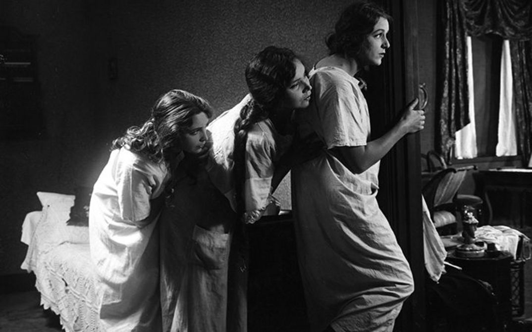 Filmstill aus NORRTULLSLIGAN: Drei junge Frauen in Nachthemden spähen durch eine Tür.