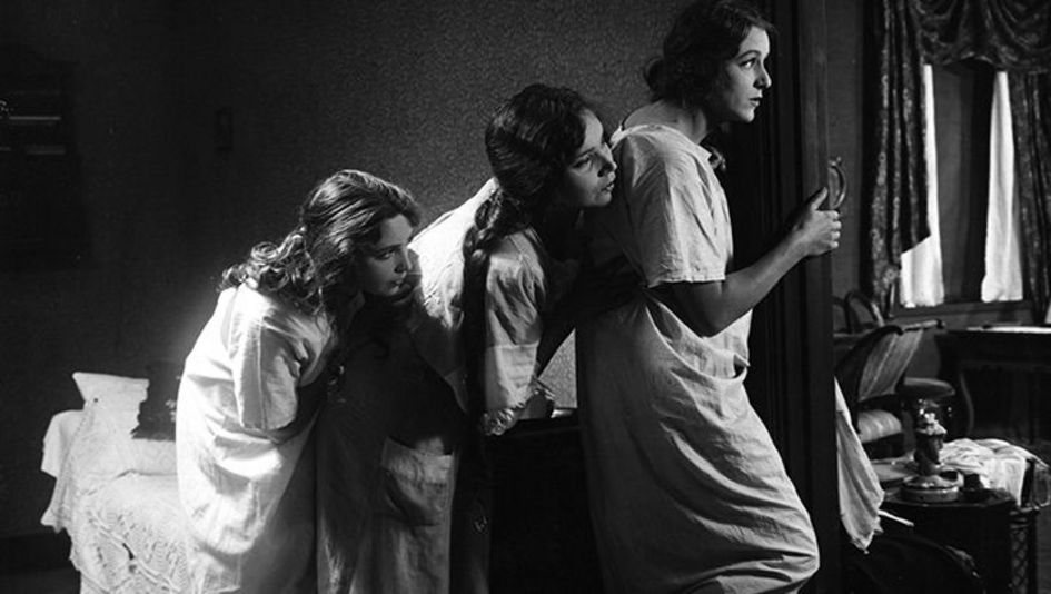 Filmstill aus NORRTULLSLIGAN: Drei junge Frauen in Nachthemden spähen durch eine Tür. 