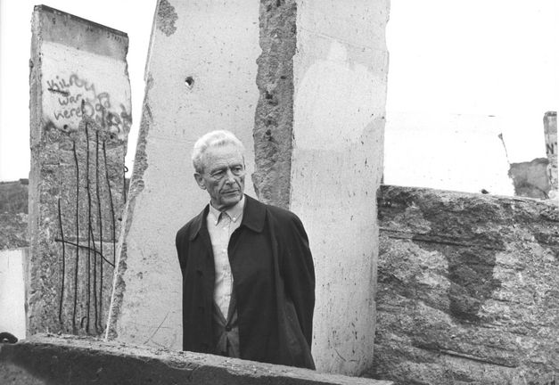 Film still from ICH WAR EIN GLÜCKLICHER MENSCH: An elderly man stands in front of the remains of the Berlin Wall.