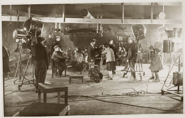 Film still from "Deda-Shvili an rame ar aris arasodes bolomde bneli" by Lana Gogoberidze. It shows a movie set filled with people. There are large lamps on the left and right. 