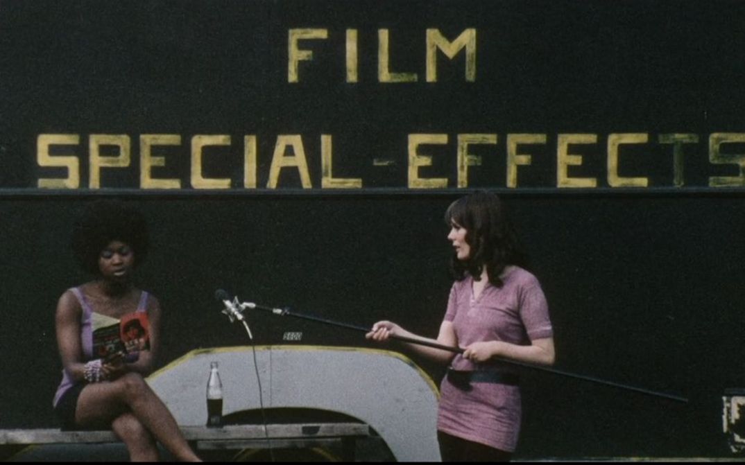 Filmstill aus DARK SPRING. Eine Frau hält einer anderen ein Mikrofon hin, die aus einem Buch liest. Im Hintergrund der Schriftzug Film Special Effects.