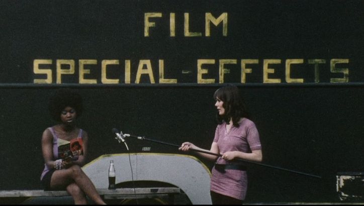 Filmstill aus DARK SPRING. Eine Frau hält einer anderen ein Mikrofon hin, die aus einem Buch liest. Im Hintergrund der Schriftzug Film Special Effects.