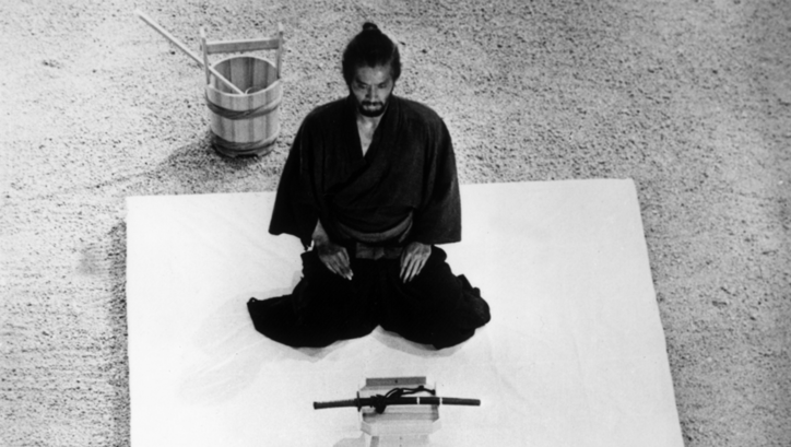 Film still from HARAKIRI: A man in a black kimono kneels in front of a sword.