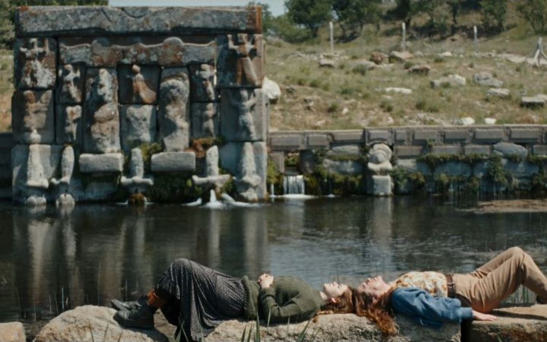 Zwei Personen liegen Kopf an Kopf auf einer steinernen Uferbefestigung, im Hintergrund ein Teich..