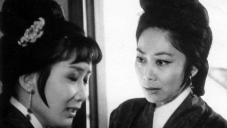 Film still from THE ARCH. Two women in historical costumes look at each other.