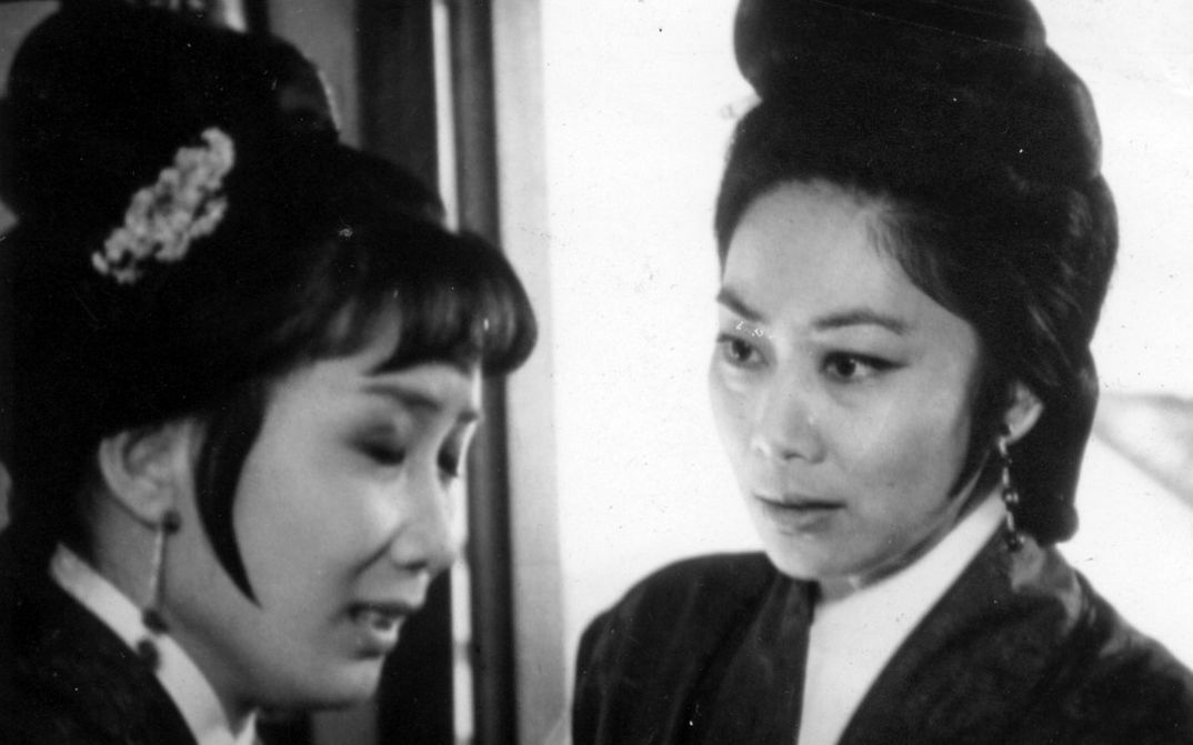 Film still from THE ARCH. Two women in historical costumes look at each other.