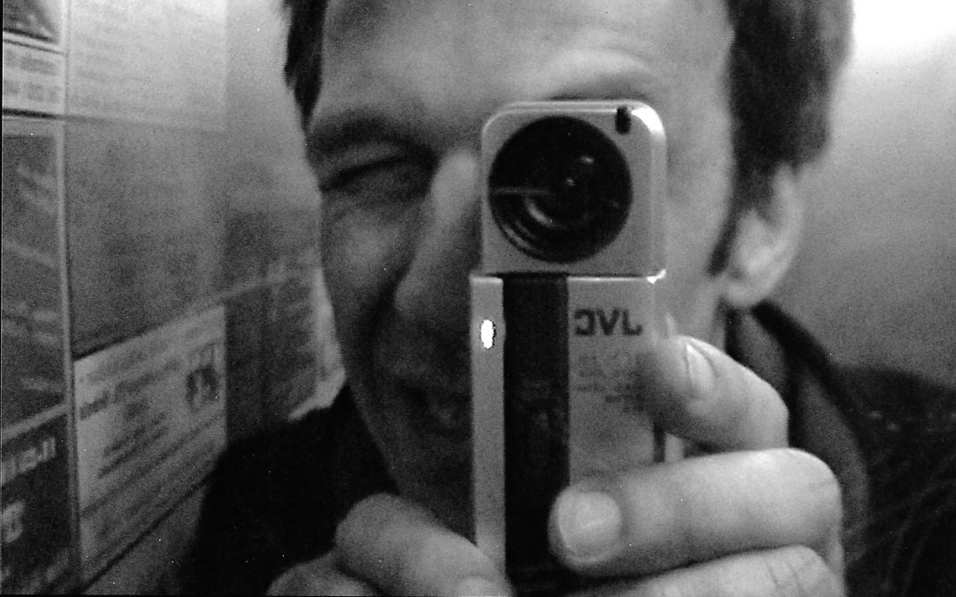 Filmstill aus killer.doc.berlin: Ein Mann hält eine kleine Videokamera vor sein Gesicht und filmt damit.