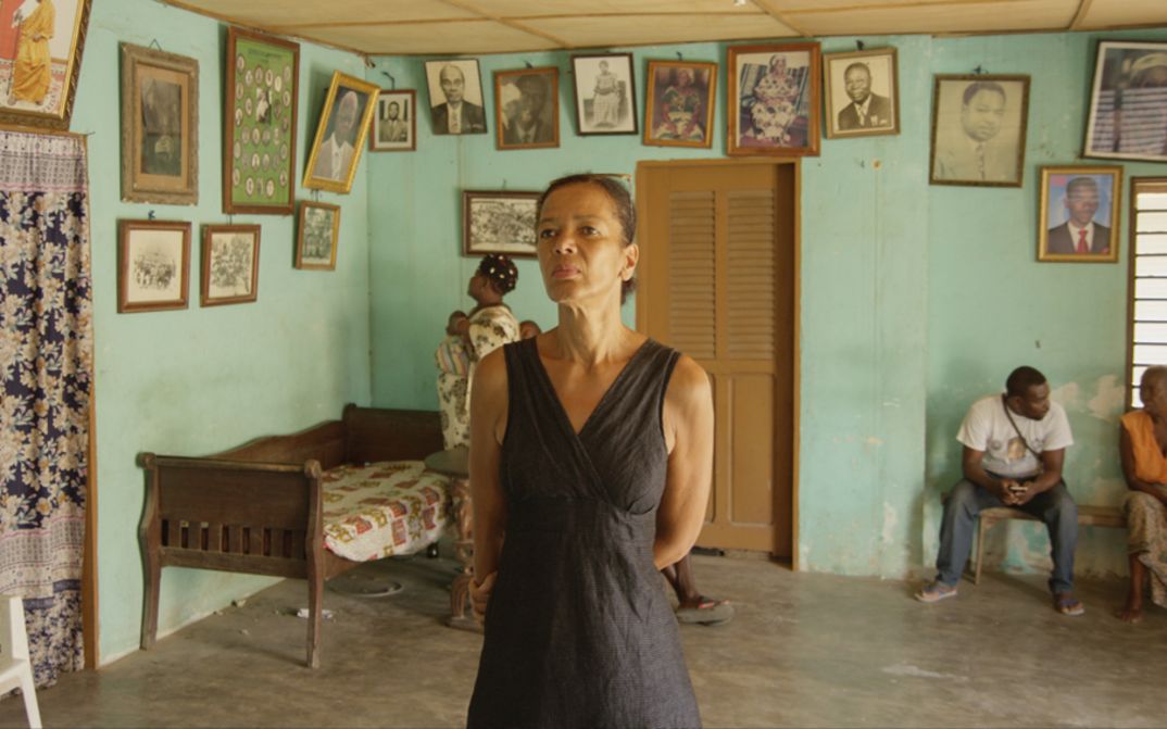 Film still from BECOMING BLACK. The filmmaker in a house in West Africa, looking at photos on the wall.