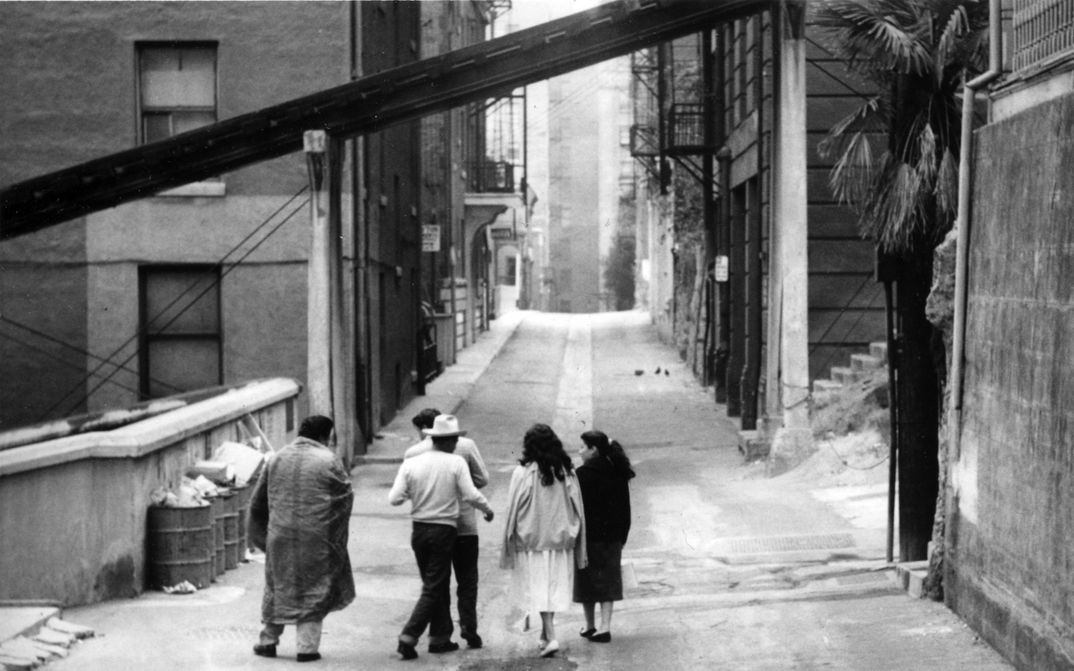 Filmstill aus THE EXILES: Eine Gruppe von Menschen geht eine ansonsten leere Straße entlang.
