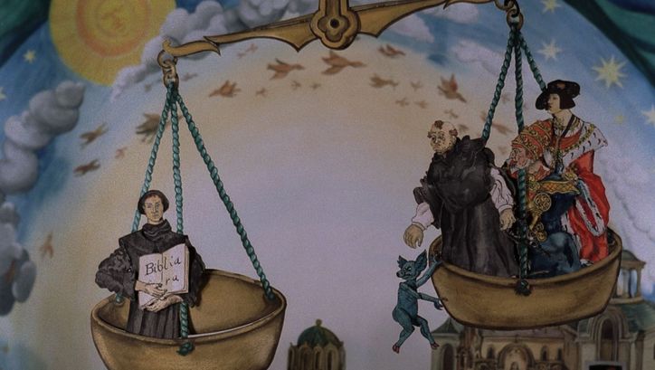 Film still from COPYRIGHT BY LUTHER: A drawing in colour. You can see a weighing pan in which church representatives and a royal person are sitting. A blue animal hangs from a bowl.