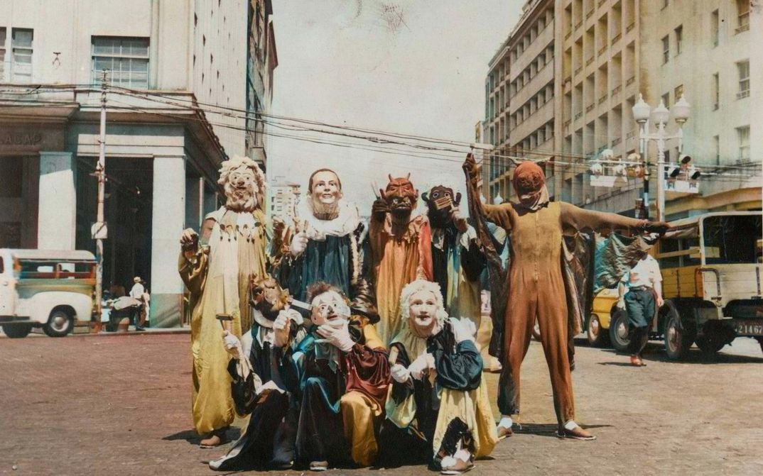 Filmstill aus PICTURES OF GHOSTS: Auf einer Straßenkreuzung posiert eine Gruppe von Menschen mit kunstvollen Masken und Kostümen.
