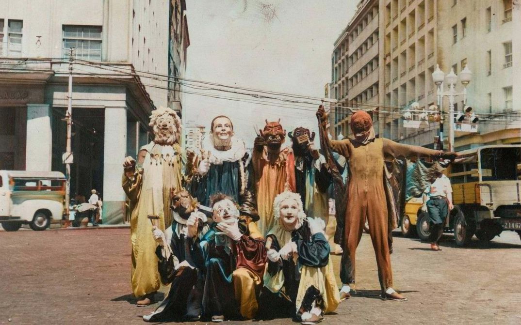 Filmstill aus PICTURES OF GHOSTS: Auf einer Straßenkreuzung posiert eine Gruppe von Menschen mit kunstvollen Masken und Kostümen.