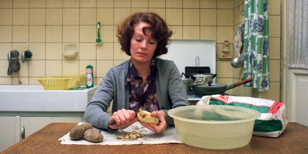 Film still from JEANNE DIELMAN, 23, QUAI DU COMMERCE, 1080 BRUXELLES: A woman is sitting at a kitchen table peeling potatoes.