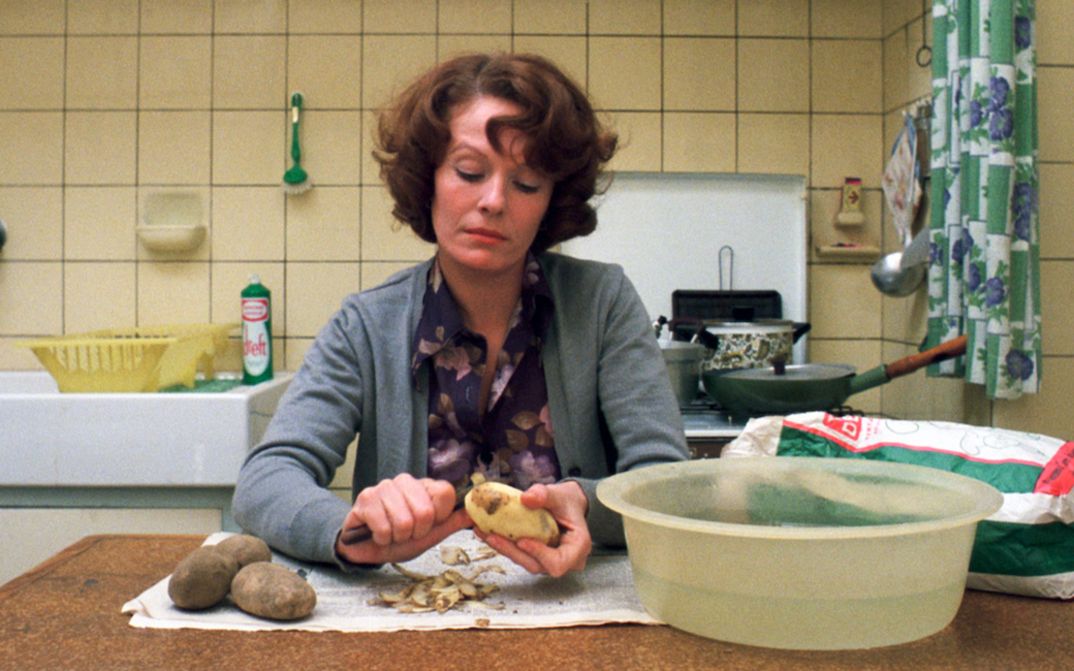 Filmstill aus JEANNE DIELMAN, 23, QUAI DU COMMERCE, 1080 BRUXELLES: Eine Frau sitzt an einem Küchentisch und schält Kartoffeln.