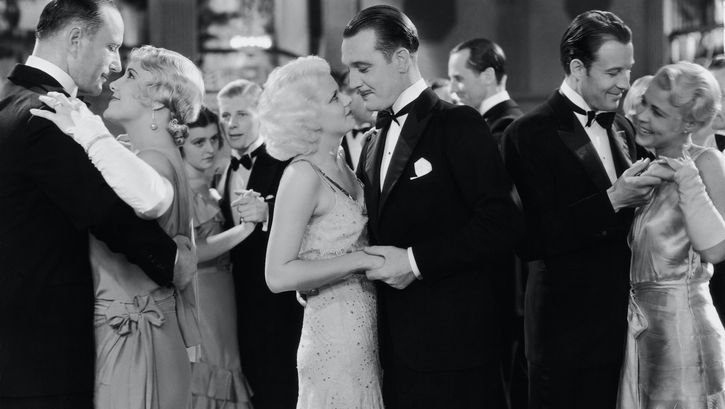 Film still from THREE WISE GIRLS: Several couples in elegant clothes dancing.