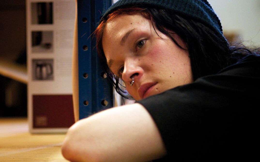 Filmstill aus SOMETHING MUST BREAK: Eine junge Person lehnt sich auf einen Tisch und blickt nachdenklich in die Ferne.