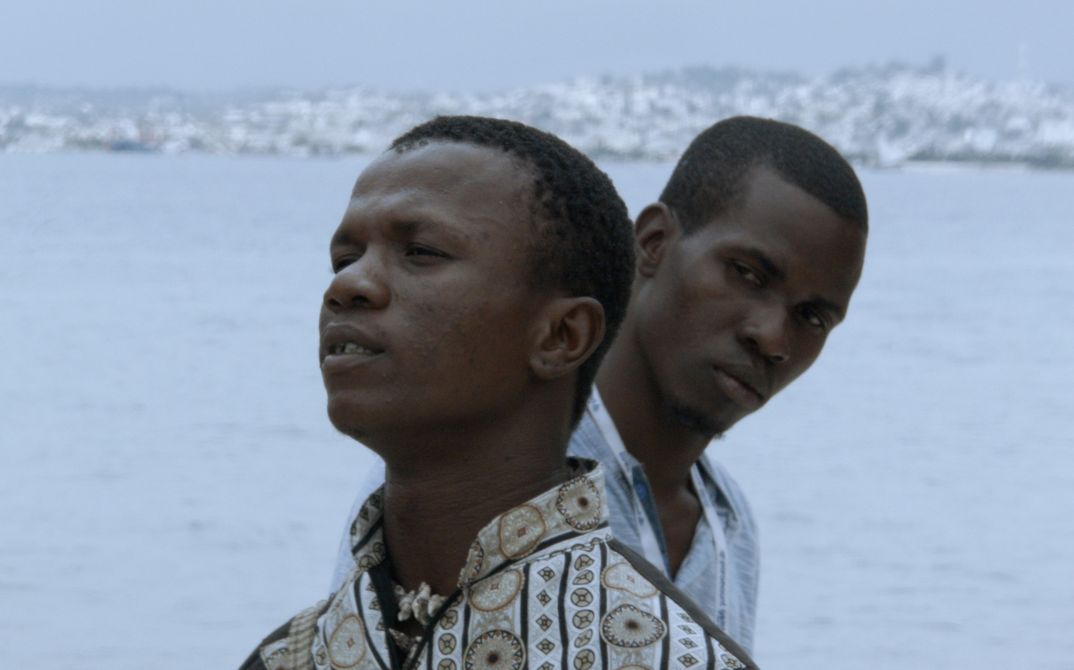 [Translate to English:] Filmbild. Die Köpfe zweier Männer vor einer Hafen-Silhouette