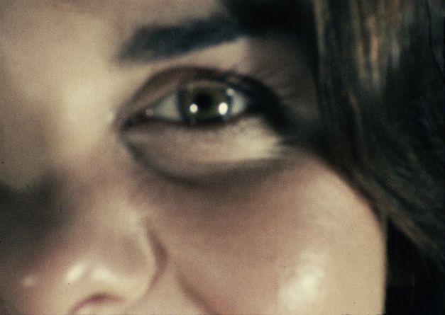 Filmstill aus "Iris" von Maria Lassnig. Zu sehen ist eine Nahaufnahme eines Gesichts, auf der nur ein Auge, Haare und ein Teil der Nase zu sehen sind.