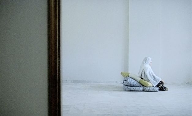 Still from the film "Beirut al lika (Beirut the Encounter)" by Borhane Alaouié. A wide shot, where a veiled woman sits alone on a mattress in a sparse apartment. 