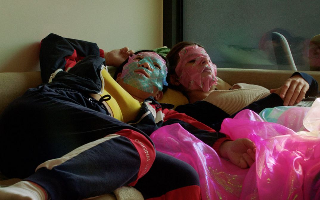 Two girls with face masks are lying on a bed in a teenager