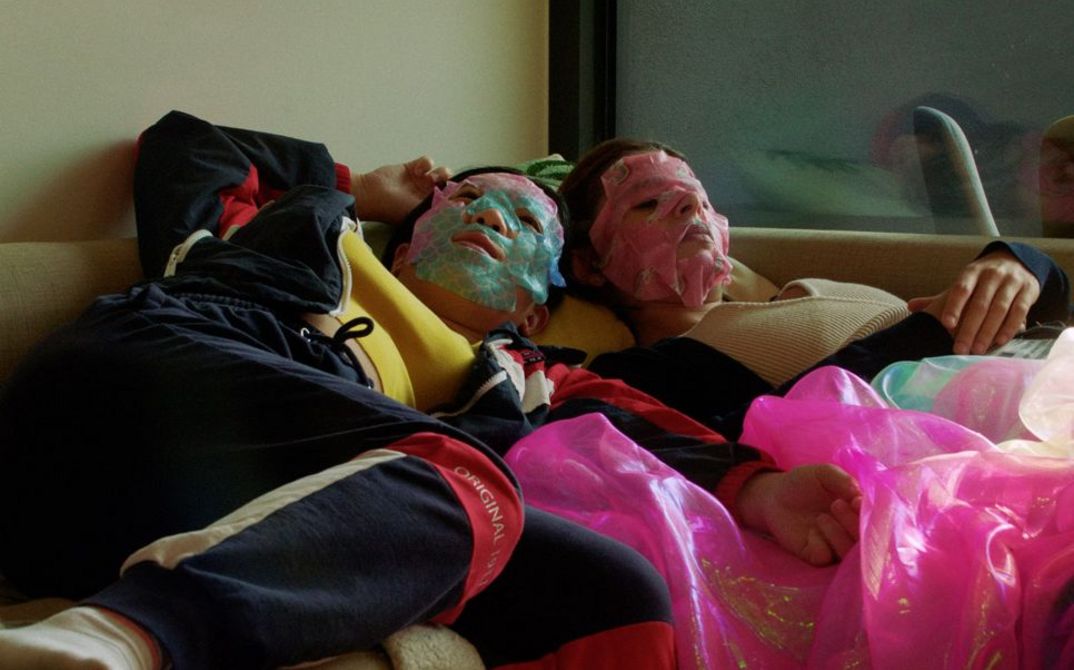 Zwei Mädchen mit Gesichtsmasken liegen auf einem Bett in einem Jugendzimmer.