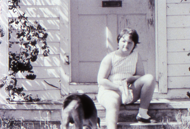 Filmstill aus LITTLE GIRL. Ein Mädchen sitzt mit ihrem Hund auf den Treppenstufen vor einem Haus.