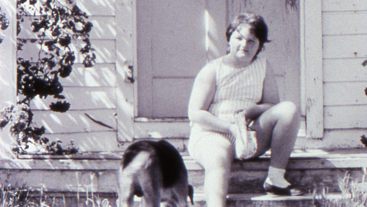 Filmstill aus LITTLE GIRL. Ein Mädchen sitzt mit ihrem Hund auf den Treppenstufen vor einem Haus.