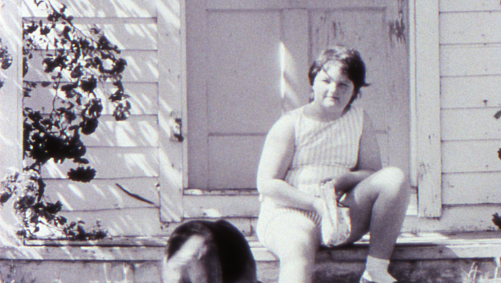 Film still from LITTLE GIRL. A girl sits with her dog on the steps in front of a house.
