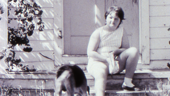 Filmstill aus LITTLE GIRL. Ein Mädchen sitzt mit ihrem Hund auf den Treppenstufen vor einem Haus.