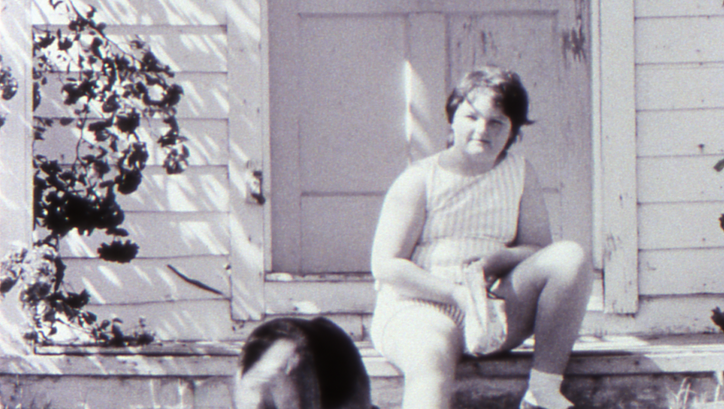 Film still from LITTLE GIRL. A girl sits with her dog on the steps in front of a house.