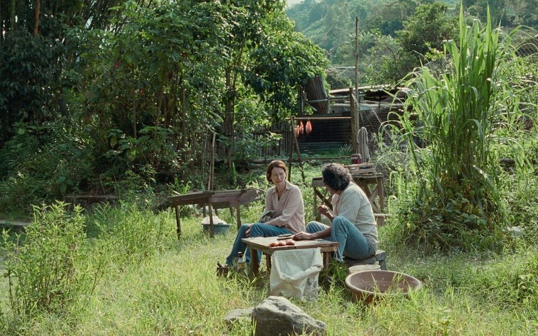 Filmstill aus MEMORIA: Zwei Menschen sitzen in einem üppig grünen Garten.