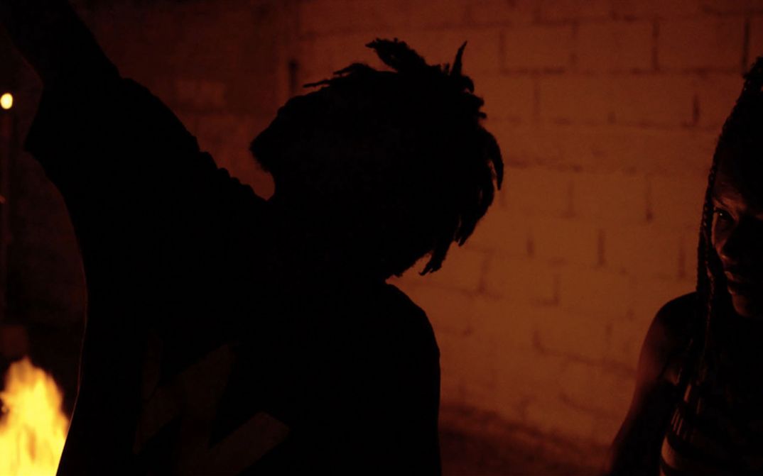 Filmstill aus dem Film "The Wake" von The Living and the Dead Ensemble. Man sieht die Silhouette einer Person im Dunkeln vor einer Ziegelwand.