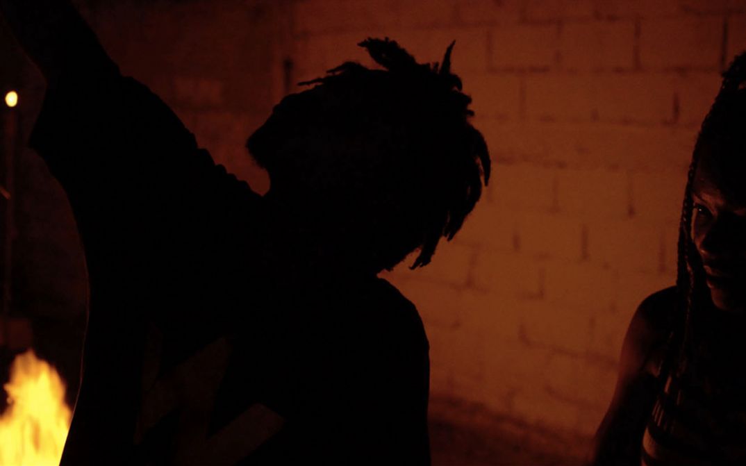 Still from the film "The Wake" by The Living and the Dead Ensemble. The silhouette of a person in the dark in front of a brick wall.