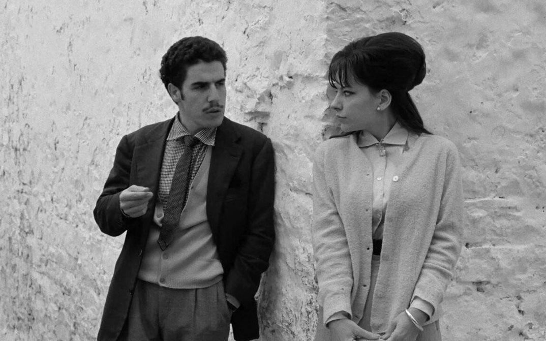 Filmstill aus I BASILISCHI: Ein Mann und eine Frau stehen an der Ecke eines Hauses und schauen sich an.