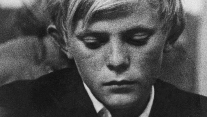 Filmstill aus HOW LONG DOES MAN LIVE: Ein Junge mit nachdenklichem Gesichtsausdruck blickt zu Boden.