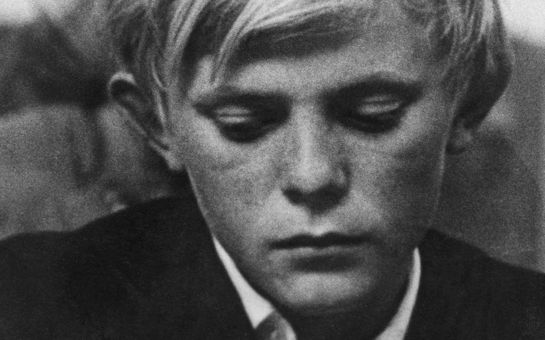 Filmstill aus HOW LONG DOES MAN LIVE: Ein Junge mit nachdenklichem Gesichtsausdruck blickt zu Boden.